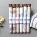 Bath salts by Whole Self Aromatherapy in test tubes displayed on a light gray background, with a yellow flower and white towels nearby.